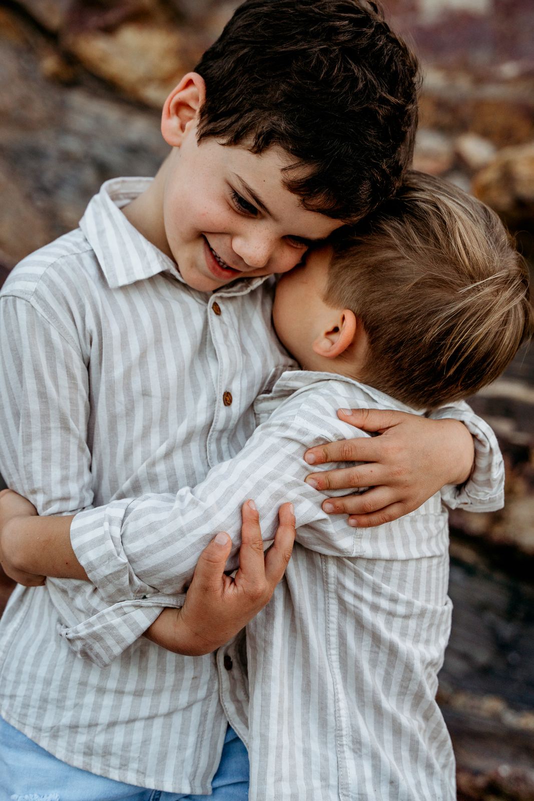 Two brothers in striped shirts sharing a big hug and laughing