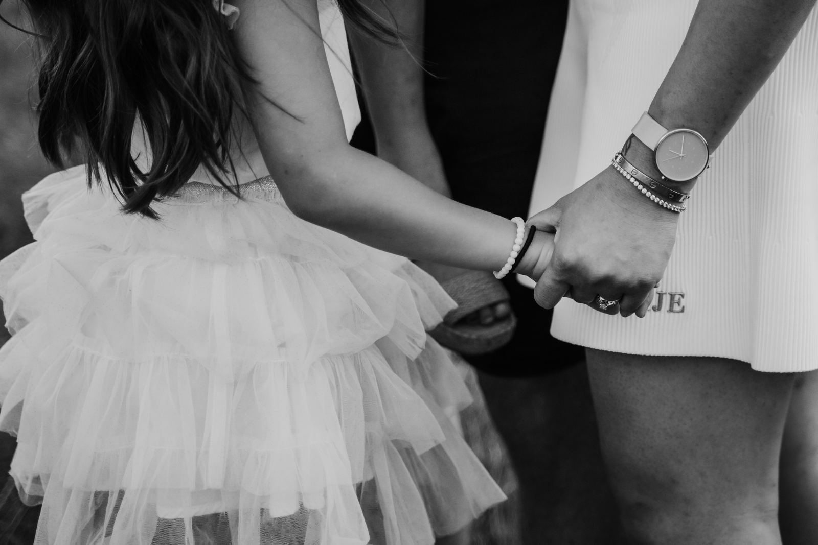 Black and white close-up of parents holding hands beside their daughter's tulle skirt