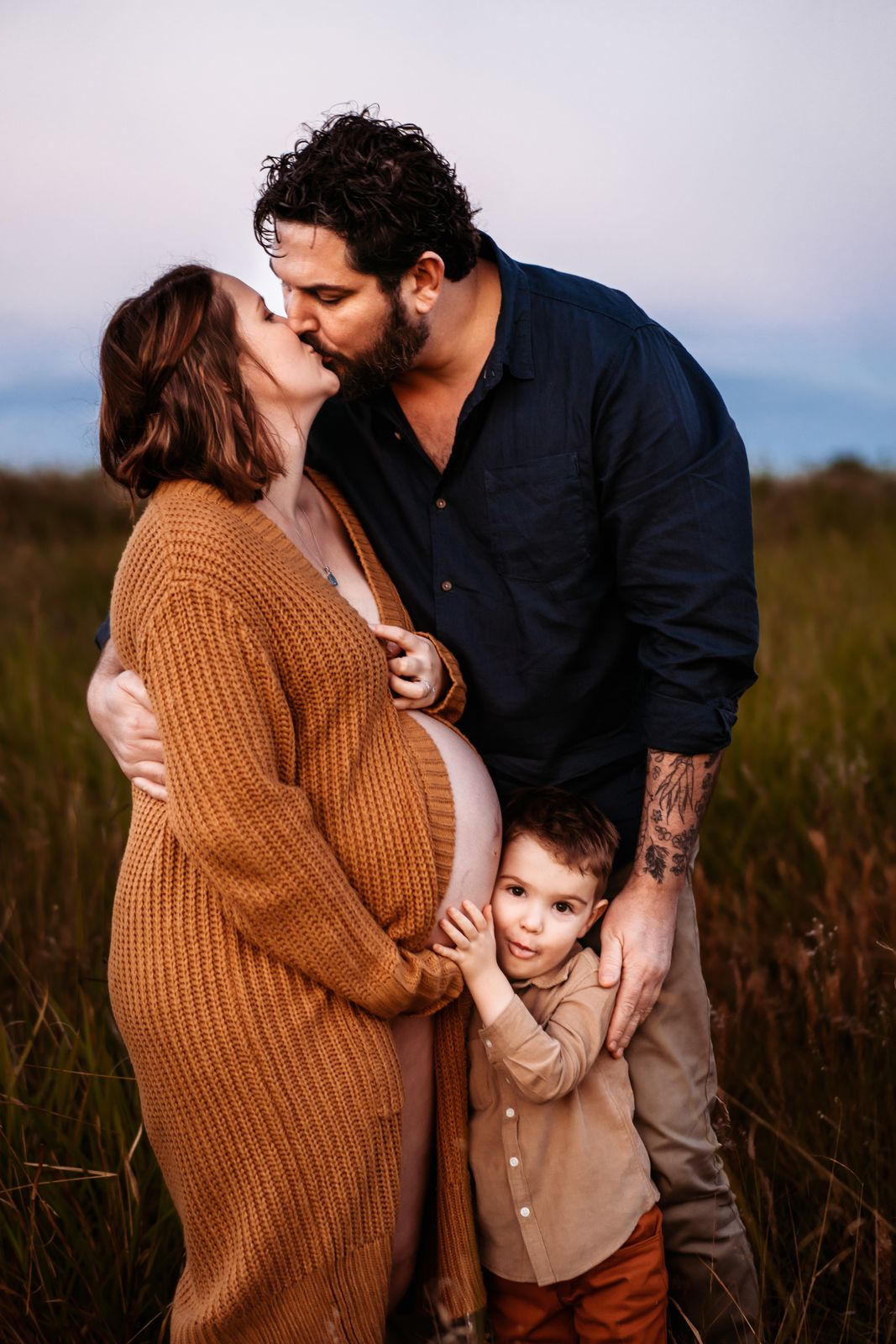 Expecting parents sharing a kiss while their son hugs mum's bump