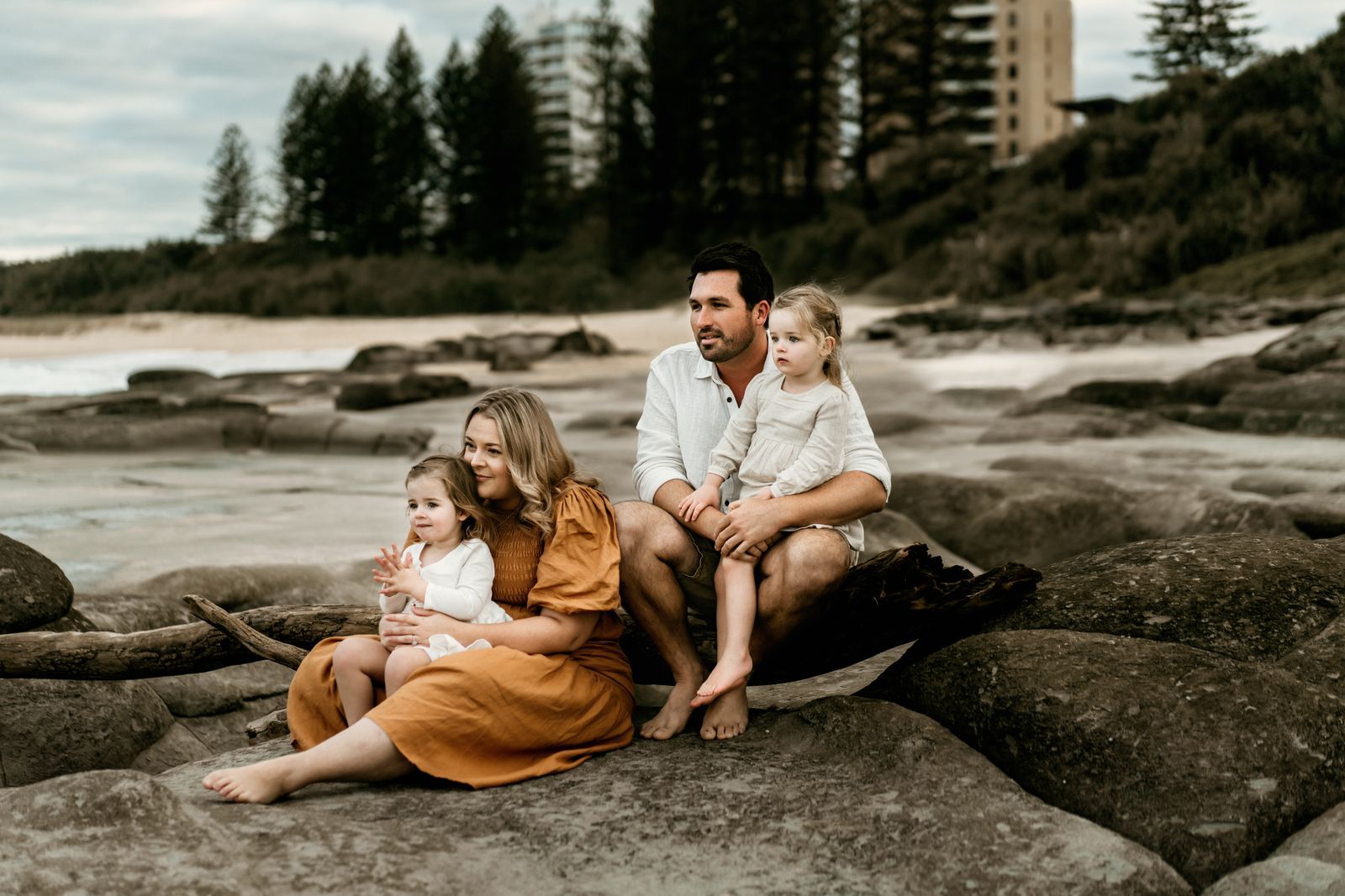 Family of four sitting together on beach rocks