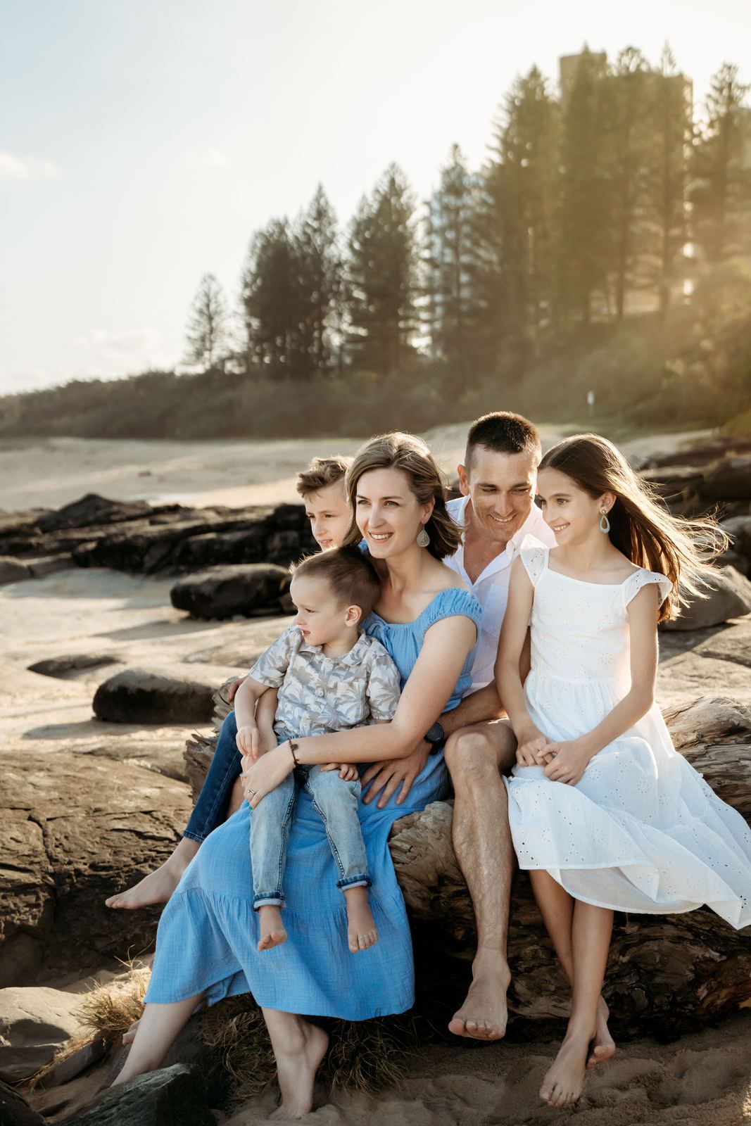Family of five sitting on beach rocks in blue and white outfits
