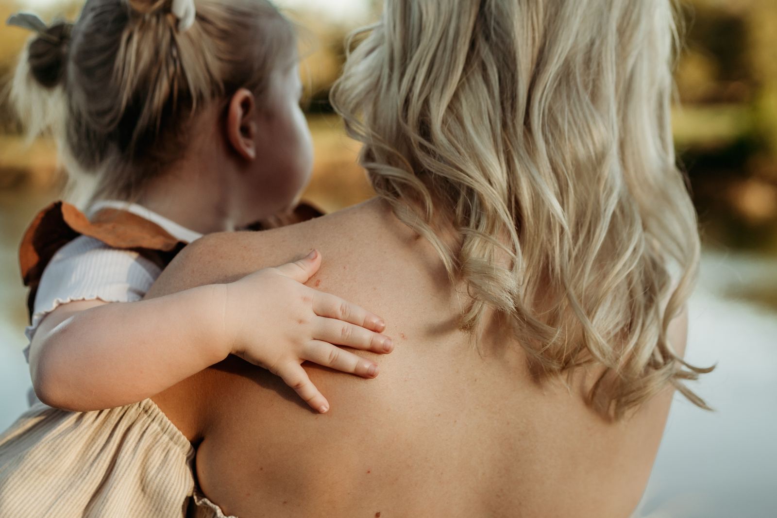 Little girl with her arm around her mum's shoulders, looking out over the water