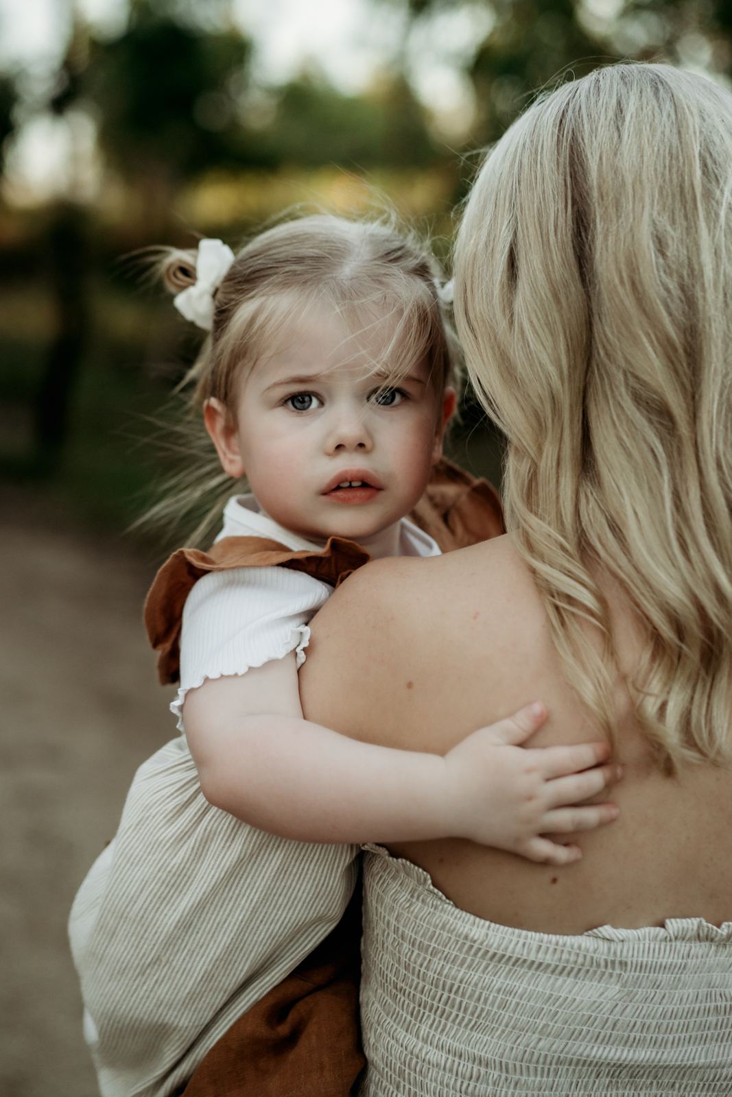 Little girl peeking over her mum's shoulder on a bush track