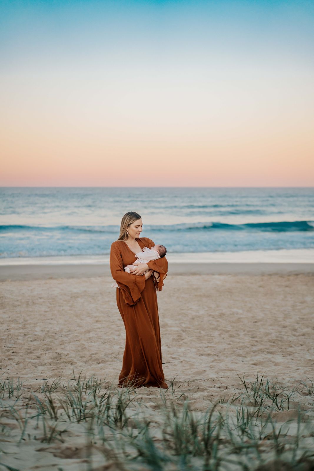 Mum holding her baby on the beach under a pastel sunset