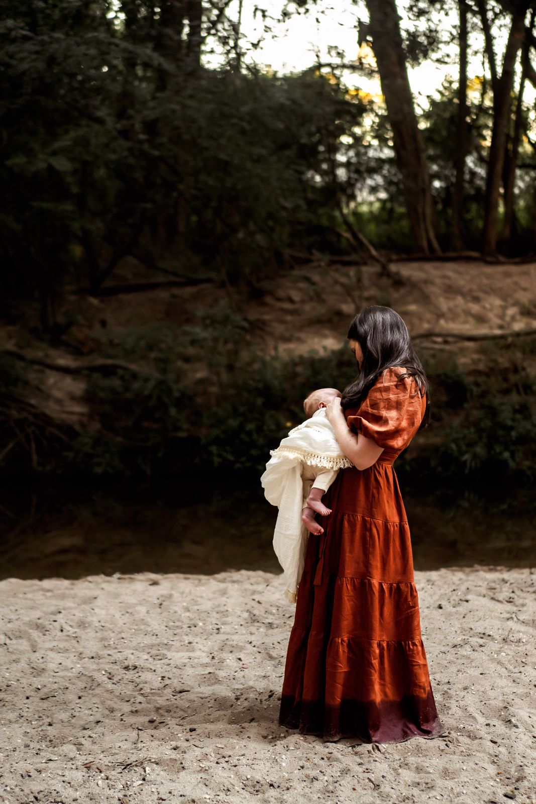 Mum in a red dress holding her baby in the bush