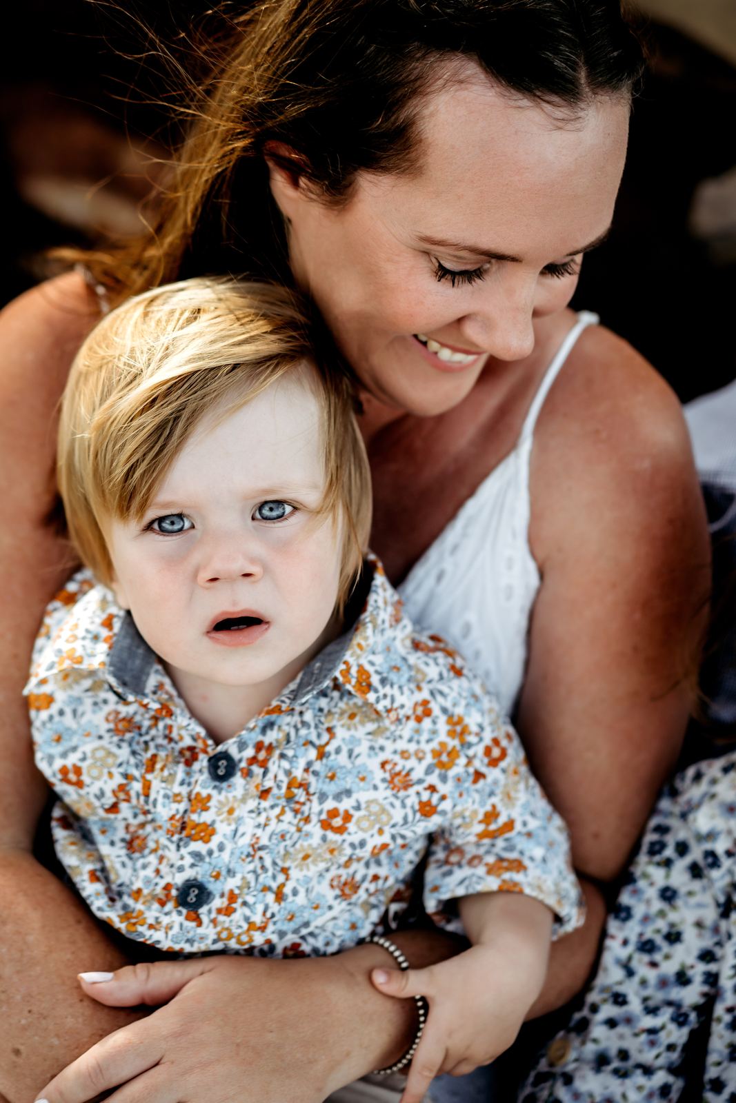 Mum smiling down at her toddler son in a floral shirt sitting on her lap
