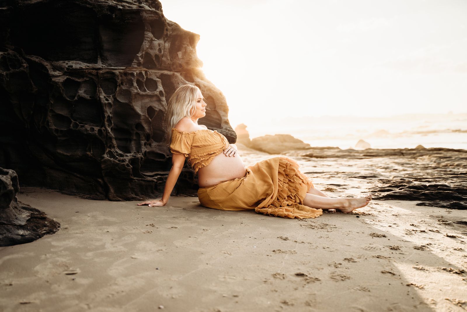 Mum-to-be lying on the sand beneath sandstone cliffs