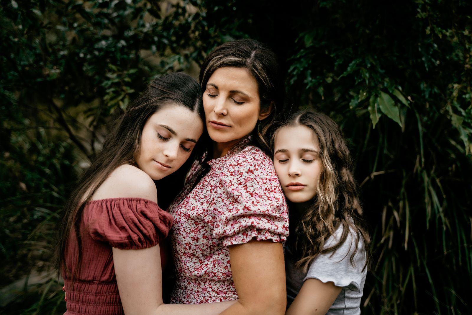 Mum with her two daughters, heads together and eyes closed