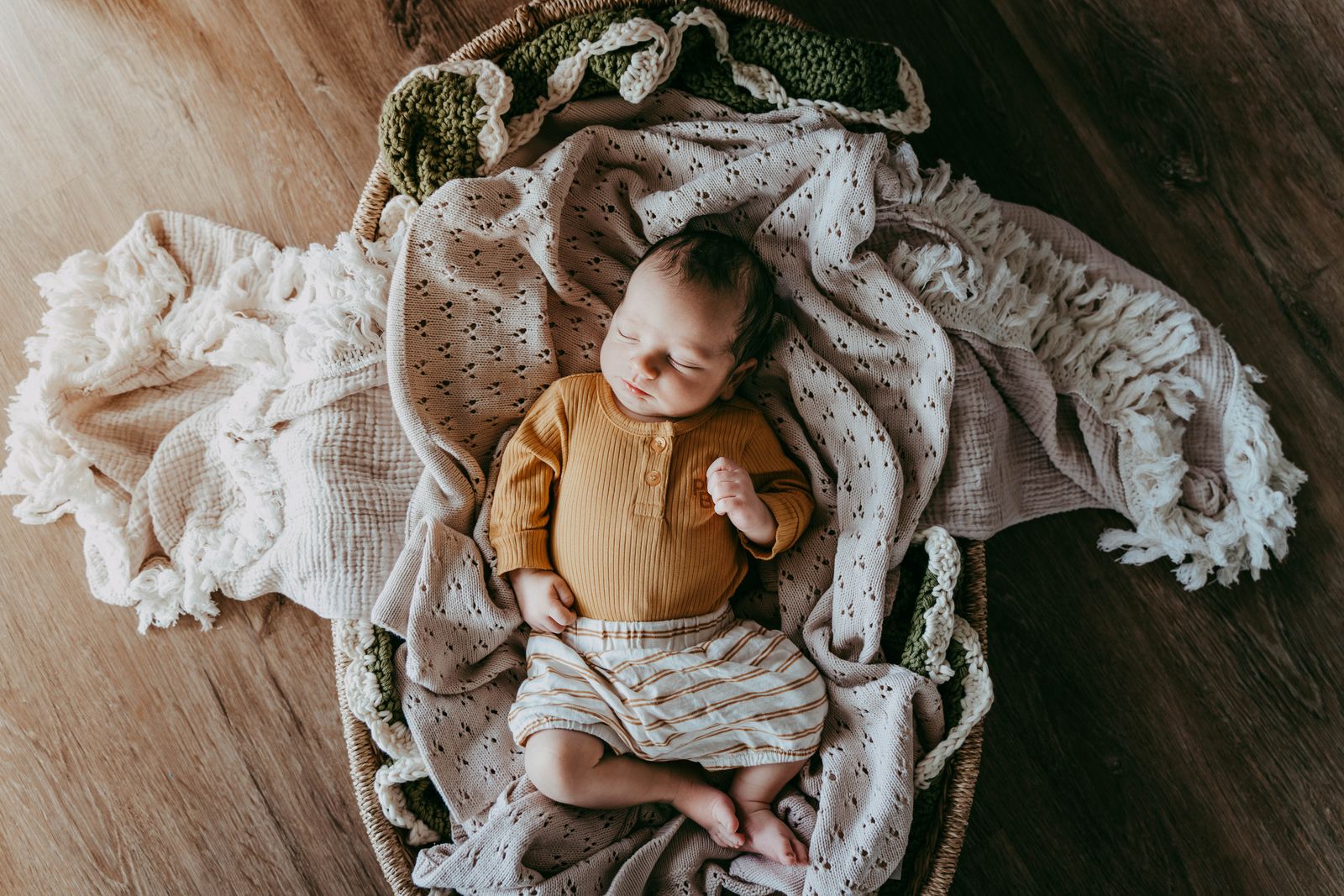Newborn curled up in a basket with a knit wrap and dried flowers